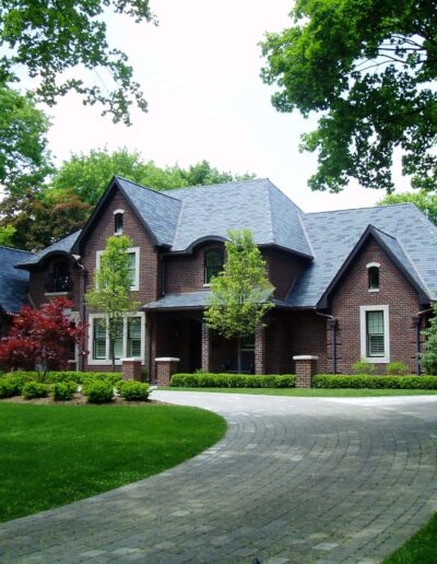 A large brick house with a curved driveway and surrounded by lush greenery.