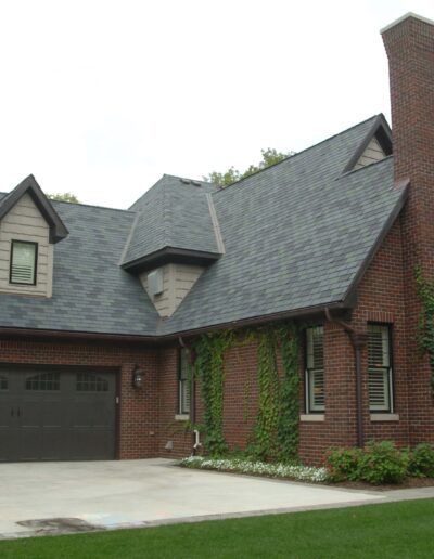 A brick house with steep gabled roofs and ivy-covered walls, featuring an attached two-car garage.