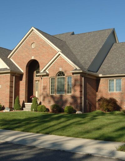 Spacious brick suburban home with a gabled roof on a sunny day.