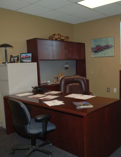 A well-organized office space with a wooden desk, chair, bookshelf, and decorative items on the walls.