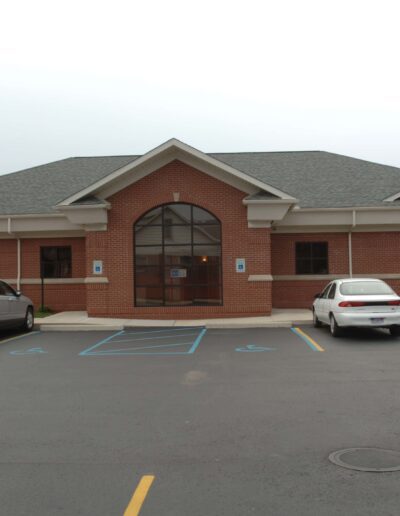 Single-story brick commercial building with a parking lot in front, featuring handicap parking spaces and two parked cars.