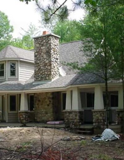 Two-story house with stone accents and a covered porch nestled in a wooded area.
