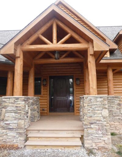 Rustic wooden cabin entrance with stone pillars and a dark wood door.